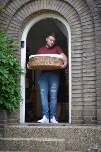 Man stood in doorway holding a moses basket.
